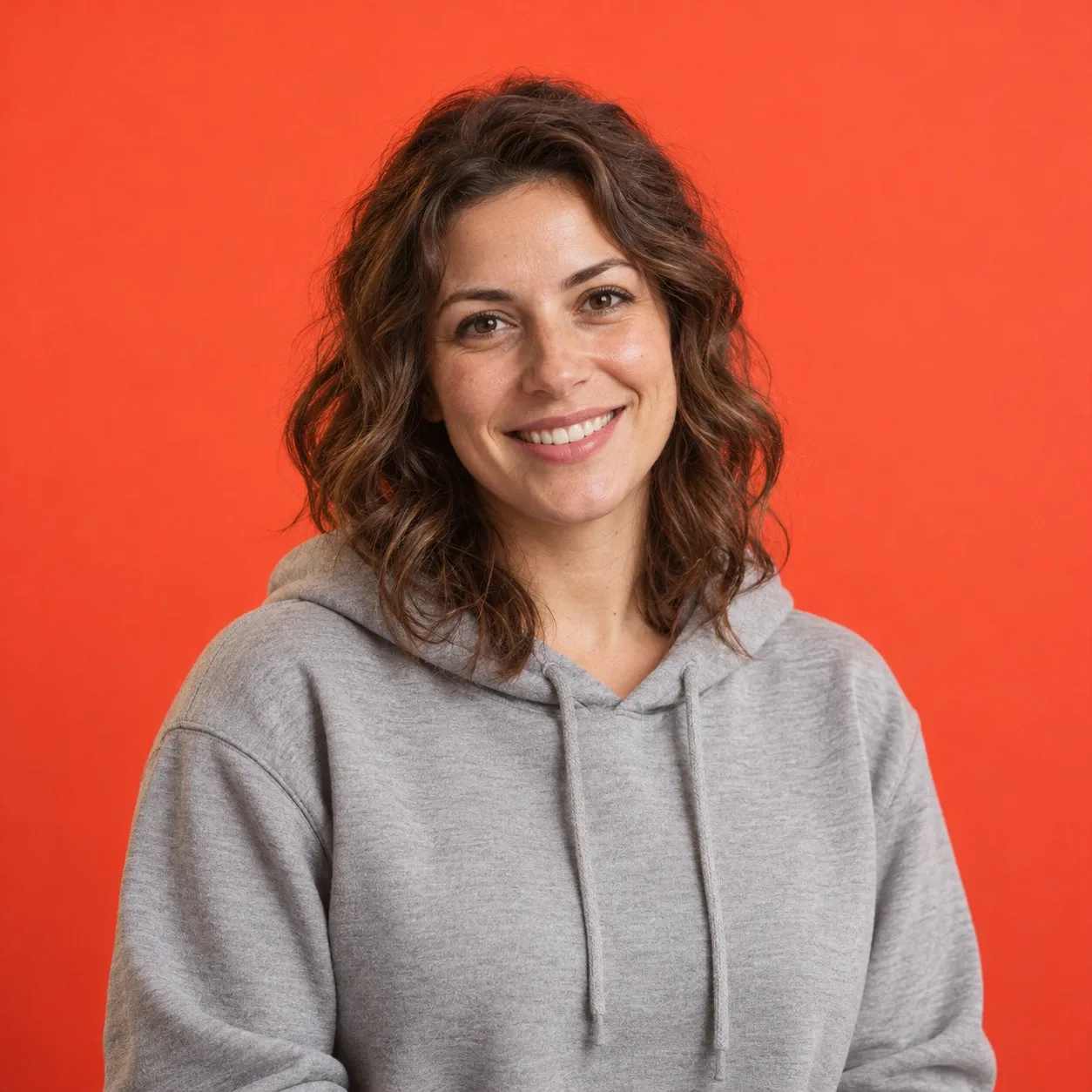Woman in her late 20s with wavy shoulder-length brown hair and a grey hoodie, chest-up