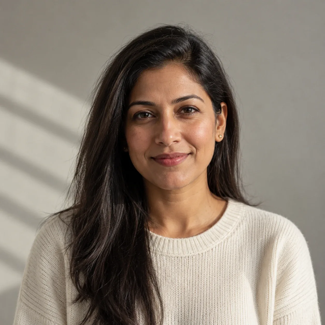 Woman in her mid-30s with long straight black hair tucked behind one ear, small gold studs