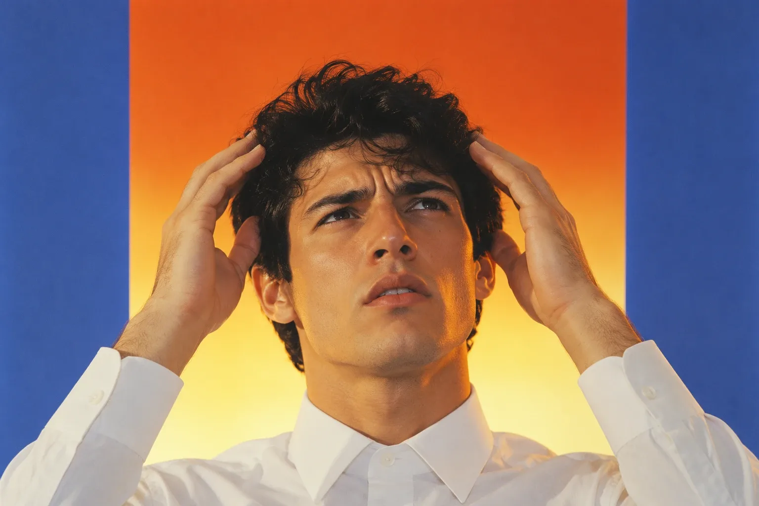 A young man with black hair holding his head with both hands