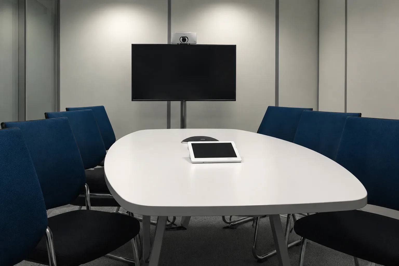 Empty modern conference room: white oval table, navy chairs, wall-mounted screen