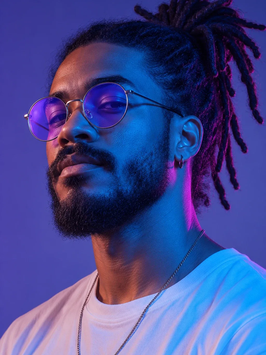 A man with dreadlocks tied up, round violet-tinted glasses and a beard