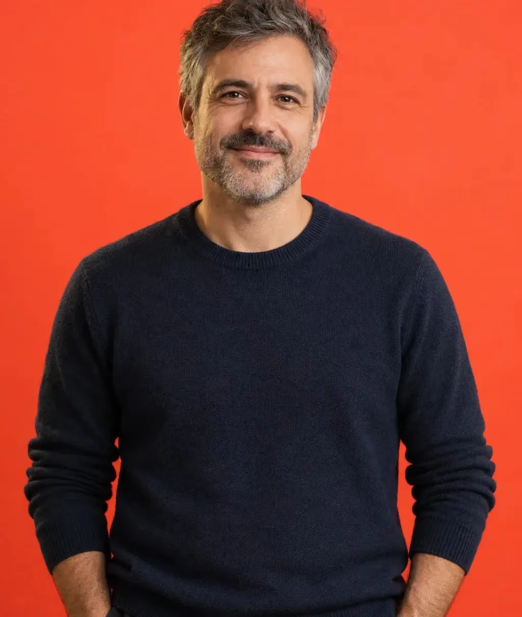 Man in his 40s with short grey hair and a navy knit sweater, hands in pockets