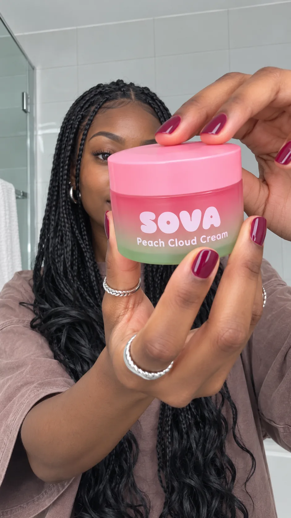 Fictional model holding a pink SOVA cream jar in a bright bathroom.