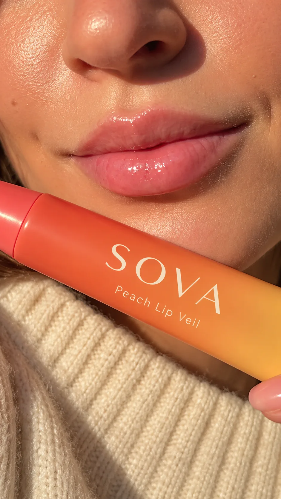 Warm editorial closeup holding SOVA Peach Lip Veil below the lips.