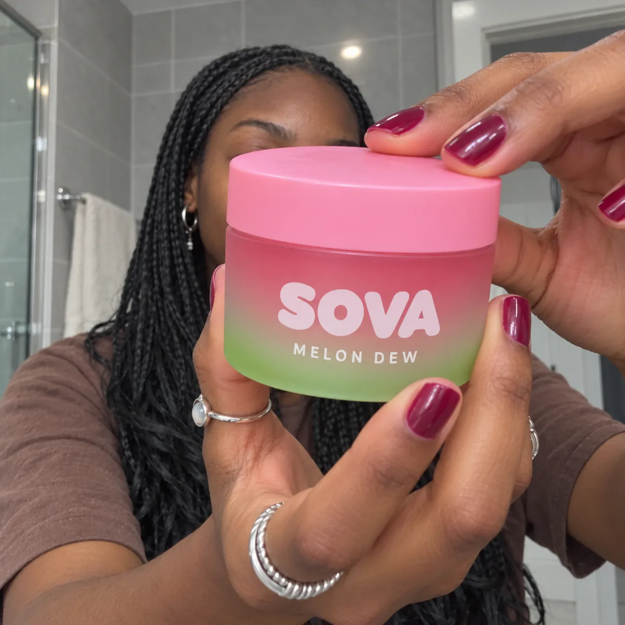 A fictional adult model with braids holding a pink-to-lime SOVA concept jar near the camera.