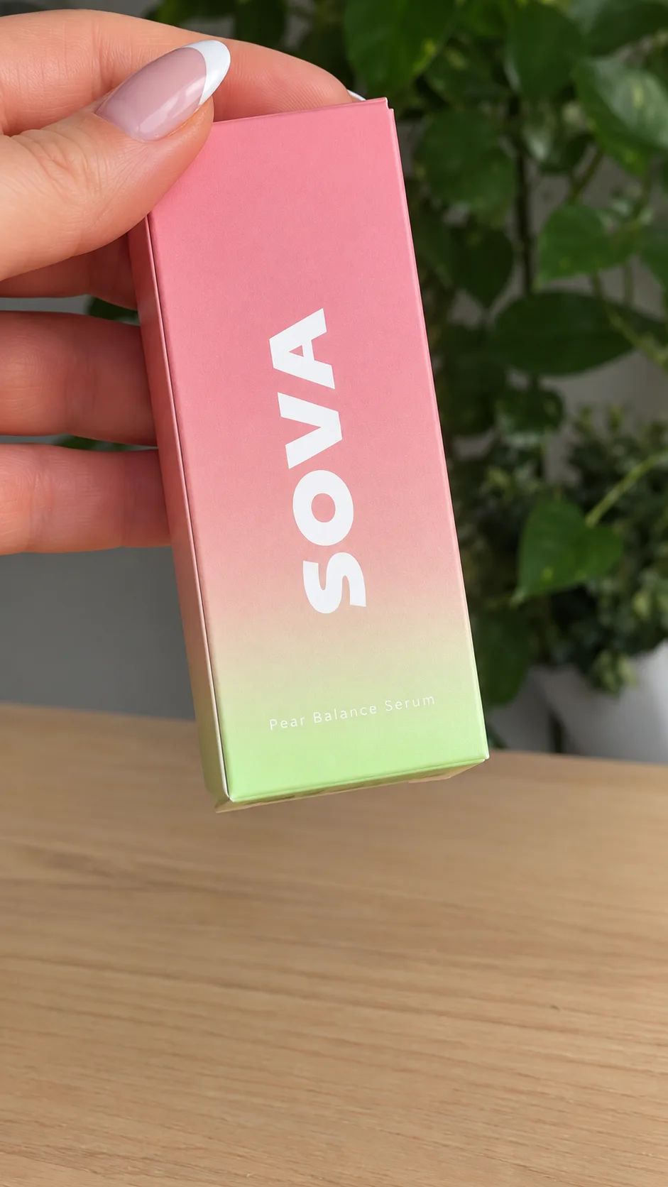 Hand holding a SOVA serum carton above a wooden table.